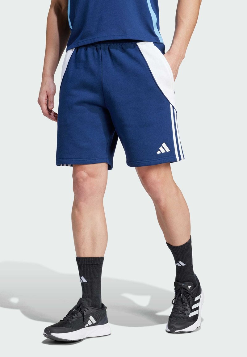 Blå sportsshorts med hvide sidepaneler, elastisk talje og tre hvide striber på underbenet. Sammen med sorte sportssko og sokker.