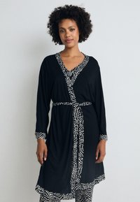 Čierne obopínacie šaty s dlhými rukávmi, opaskom v páse a kontrastným bielym vzorovaným lemovaním okolo výstrihu a rukávov. Mäkká textúra.