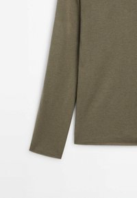 Haut à manches longues vert olive confectionné dans un matériau doux et texturé avec un col rond et un ourlet droit. Design simple et épuré.