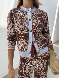 Brauner Cardigan mit weißem Paisleymuster, blauem geripptem Kragen und Bündchen, roten Akzenten und braunen Knöpfen. Getragen mit passenden Hosen.