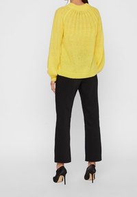 Yellow knitted sweater with a ribbed texture, oversized balloon sleeves, and a round neck. Paired with black tailored pants and high heels.