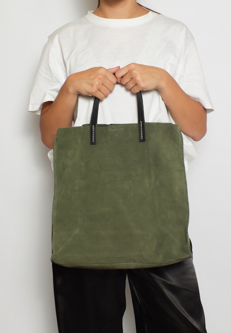 Olijfgroene suede tote bag met zwarte leren handvatten, rechthoekige vorm, zichtbare stiksels en strakke lijnen. Geschikt voor casual gebruik.