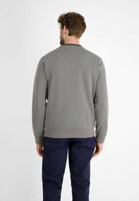 Szara bluza z okrągłym dekoltem i ściągaczami przy rękawach, noszona z granatowymi spodniami. Gładka tkanina i prosty fason, bez widocznych logo czy wzorów.