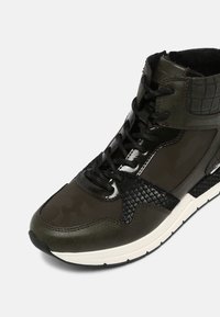 Sneaker alta di colore verde oliva scuro, caratterizzata da una combinazione di materiali testurizzati, dettagli neri e una suola bianca. Lacci neri.