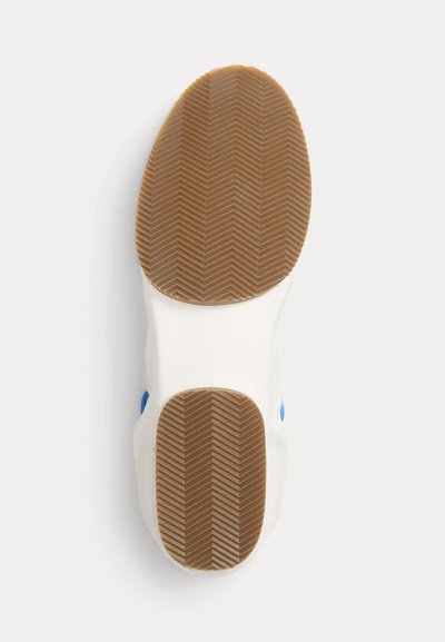 Suela de una zapatilla blanca con suela exterior de goma marrón que presenta un patrón de dibujo en espina de pescado, vista desde abajo sobre un fondo liso.