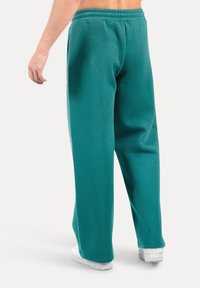 Teal joggings gemaakt van zachte stof, met een ontspannen pasvorm, elastische tailleband en zijzakken, gecombineerd met witte sneakers.