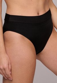 Högmidjad svart bikiniunderdel gjord av texturerad, ribbad tyg. Har en bred midjeresår och sitter ovanför höfterna.