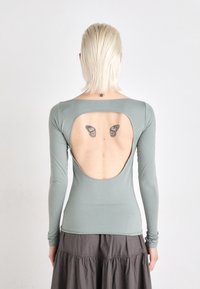 Long-sleeve, mint-green top with a large cutout at the back, made of soft, stretchy fabric. Includes butterfly tattoos visible on the skin.