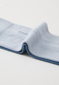 Țesătură ribbed de culoare albastră deschisă, pliată la mijloc, cu margini de culoare albastră închisă. Textură moale, cu detalii de cusătură și logo-ul "Calvin" imprimat vizibil.