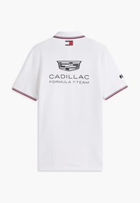 Λευκό πόλο με κόκκινη και μαύρη λεπτομέρεια, λογότυπο Cadillac και κείμενο "Cadillac Formula 1 Team" στην πλάτη, ετικέτα Tommy Hilfiger στον γιακά.