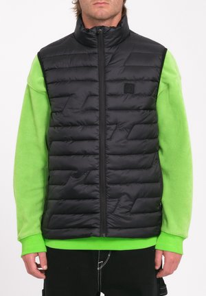 Black padded vest with a high collar, featuring geometric stitching details, worn over a bright green long-sleeve shirt.