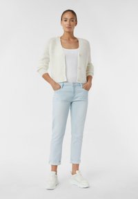Cream knitted cardigan with button closure, paired with light blue cuffed jeans and white sneakers. Smooth texture, relaxed fit, casual style.