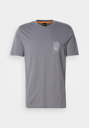 T-shirt in cotone grigio con scollatura rotonda, maniche corte e stampa grafica sulla parte sinistra del petto. L'etichetta interna presenta accenti arancioni.