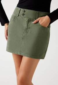 Fustă mini din denim verde, cu închidere prin două butoane, buzunare laterale și un material ușor texturat pentru un plus de detaliu.