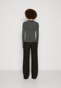 Langermet, tettsittende, mørkegrå topp med rund hals, sammen med høytlivet, løse svarte bukser. Glatt tekstur, minimalistisk design.