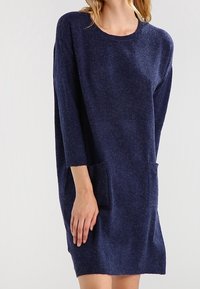 Mörkblå stickad klänning med trekvartslånga ärmar, rund halsringning och två framfickor. Mjuk textur och avslappnad, stor passform.