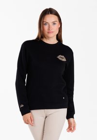 Sudadera negra hecha de tejido suave, con un diseño de labios con estampado de leopardo en el pecho y "sonríe" bordado en dorado en el puño.