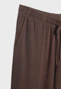 Brown fabric pants with elastic waistband, side pocket, and drawstring detail on a plain light background.