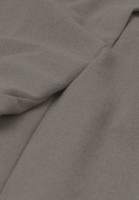 Grijze, zachte en gestructureerde stof met een matte afwerking, die zachte plooien en kreukels toont voor extra dimensie en diepte.