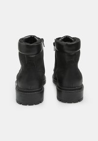 Botas negras hasta el tobillo con un acabado de ante texturizado y cuero liso, que cuentan con un cuello acolchado y cremalleras laterales para facilitar su uso.