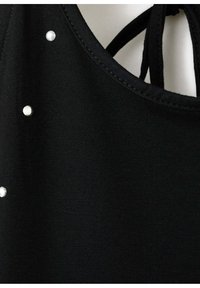 Gros plan sur un tissu noir avec des clous argentés et un décolleté avec des bretelles noires nouées à l'arrière.