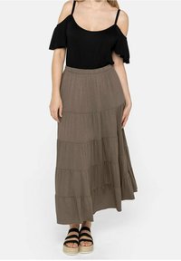 Top negro de hombros al aire combinado con una falda marrón de longitud tobillo y con volantes. La ropa tiene una textura suave y un corte relajado, complementada con sandalias negras.