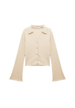 Cardigan court à manches longues texturé beige avec des manches évasées, un col et une fermeture par bouton à l'avant.