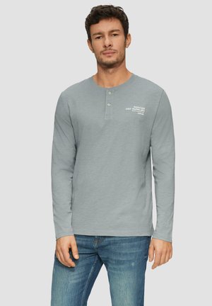 Grijze lange mouwen henley shirt gemaakt van zachte stof. Heeft een ronde halslijn en een twee-knopen sluiting met bedrukte tekst op de borst.