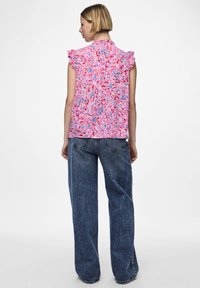 Top senza maniche floreale con spalle arricciate, caratterizzato da uno sfondo rosa con motivi astratti blu e rossi. Indossato con jeans in denim larghi.