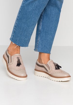 Beżowe buty ze skóry i zamszu z ozdobnymi frędzlami i perforowanymi akcentami. Gruba biała podeszwa; zestawione z przetartymi dżinsami z denimu.