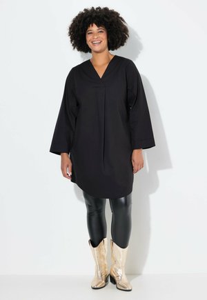 Tunic nera con scollo a V e maniche a tre quarti, abbinata a leggings neri lucidi e stivali da cowboy metallici oro.