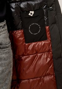 Intérieur de veste matelassée noir, rouge et gris foncé avec une poche en tissu noire étiquetée "Comment prendre soin de moi - étiquette d'entretien à l'intérieur."