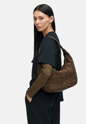 Kobieta z długimi ciemnymi w�łosami, ubrana w czarno-brązowe warstwowe rękawy, niesie dużą brązową plecioną skórzaną torbę na ramię.