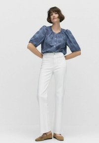 Blå texturerad blus med puffärmar och knäppning, ihop med högmidjade vita byxor och bruna lågskor.