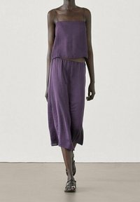 Lila zwei-teilige Kleidung mit einem Cropped-Top und leichten, fließenden weitem Hosen. Der Stoff scheint weich zu sein und hat eine subtile, strukturierte Oberflächenbeschaffenheit.