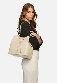 Borsa a secchiello in pelle beige con chiusura a coulisse, forma strutturata e due spallacci. Superficie testurizzata con minimi accenti in metallo.