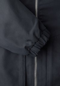 Czarny rękaw kurtki z elastycznym ściągaczem na zamku błyskawicznym w kolorze srebrnym na czarnej tkaninie.