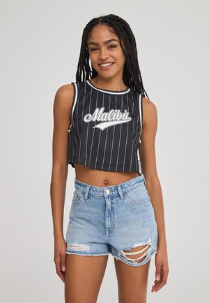 Top corto nero a righe bianche con la scritta "Malibu" stampata sul davanti; abbinato a pantaloni shorts in denim chiaro con effetto strappato.