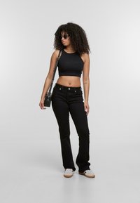 Top corto negro y vaqueros negros acampanados. El conjunto se acompaña de zapatillas color tostado y gafas de sol redondas y oscuras. Accesorios mínimos.