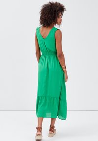 Robe sans manches verte avec un dos en V, taille élastique et ourlet en étages. Fabriquée en tissu léger, avec une texture lisse et une silhouette fluide.