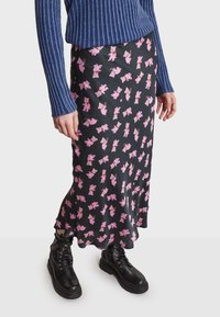 Černá sukně s hravým vzorem růžových medvědů a vlnitým lemem. S kombinací modrého žebrovaného svetru a černých šněrovacích bot.