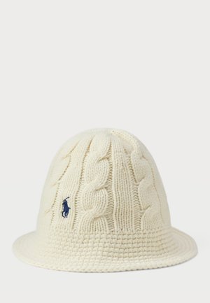 Cream knitted hat with a cable design, circular brim, and textured finish. Features a small embroidered logo in dark blue.