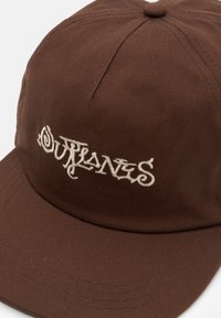 Brun keps tillverkad av texturerat tyg, med en broderad vit "Surlanes"-logotyp på framsidan, curvad skärm och sömnadsdetaljer.