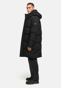 Zwarte gewatteerde parka met een hoge kraag en capuchon, voorzien van een ritssluiting, zijzakken en een logo patch op de arm. Gelaagd stof.