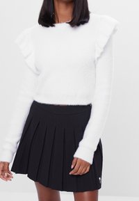 White fuzzy sweater with ruffled sleeves, paired with a black pleated skirt. The sweater features a cropped design and long sleeves.