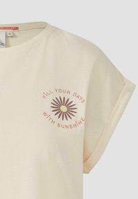 Lichtbeige t-shirt met een ronde halslijn en opgerolde mouwen. Voorzien van een grafiek van een bruine zonnebloem en de tekst "Vul je dagen met zonneschijn."