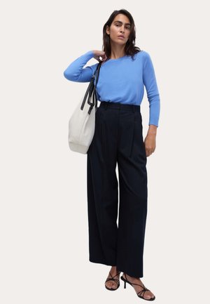 Maglione azzurro chiaro a maniche lunghe abbinato a pantaloni neri a righe sottili a vita alta. Scarpe con tacco nere con cinturini e borsa bianca con dettagli neri.