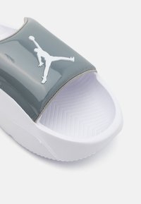 Grå patent slide sandal med hvid gummisål. Har et fremtrædende hvidt Jordan-logo på overkappen og en tekstureret indersål.
