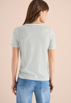 Kobieta zwrócona tyłem, ubrana w białą koszulkę z krótkim rękawem z cienkimi czarnymi poziomymi paskami oraz jasnoniebieskie dżinsy.