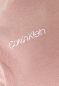 Růžová tkanina s ribbovanou strukturou a bílým logem "Calvin Klein" vytištěným na ní.